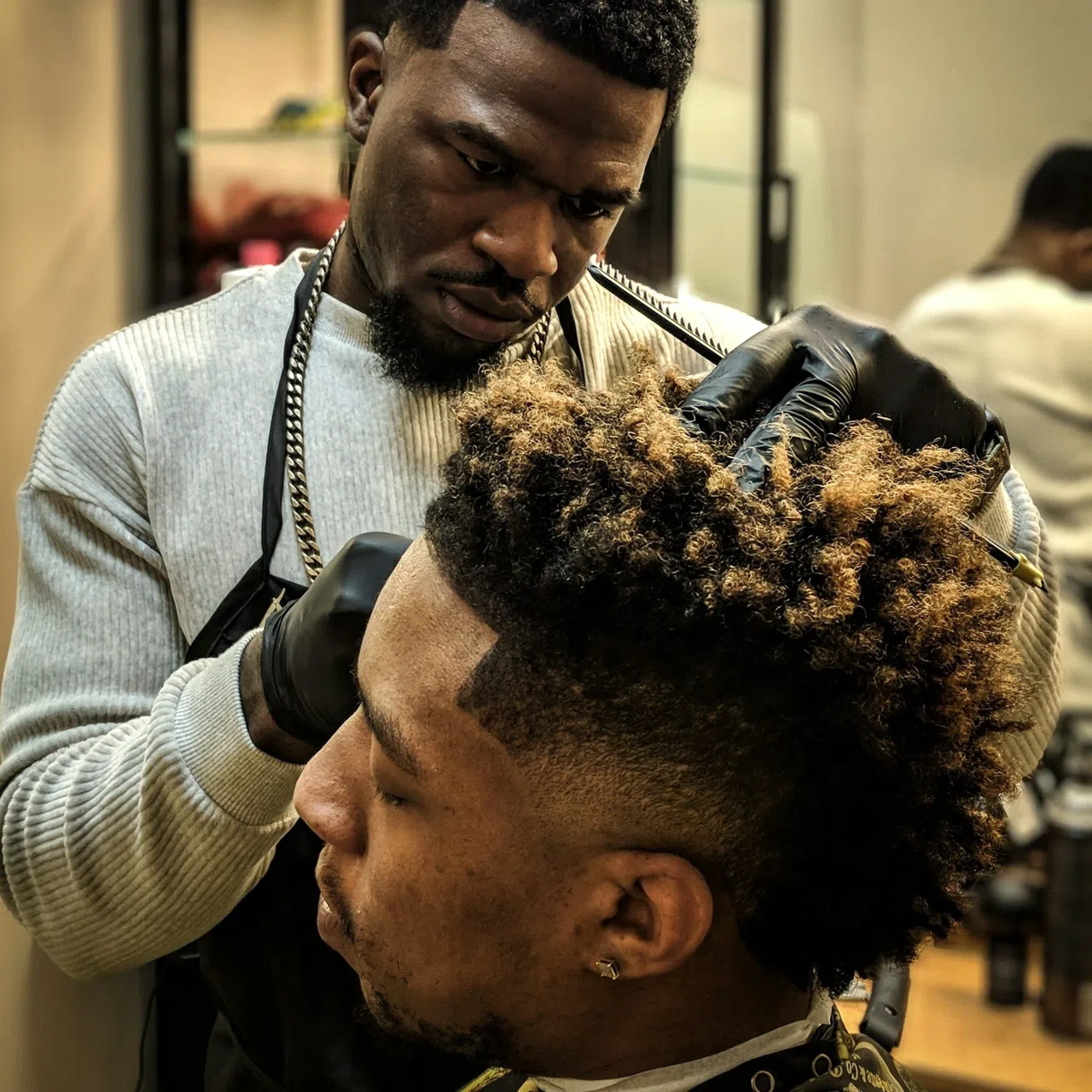 Un barbier termine un dégradé sous un dessus bouclé.